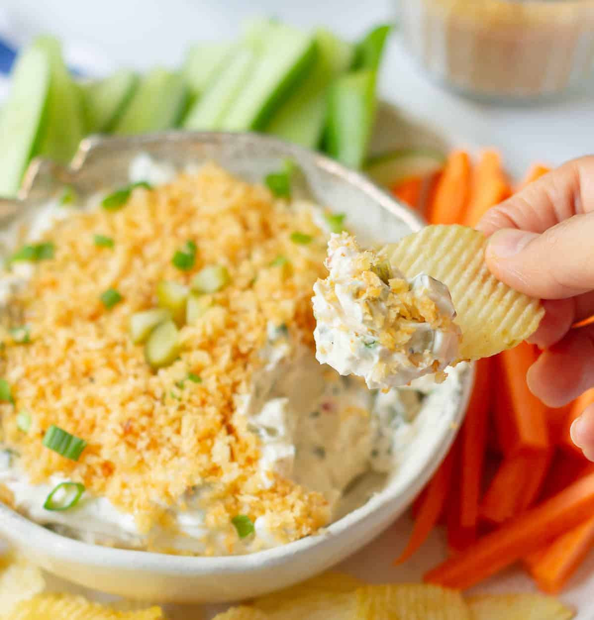 A hand scooping out dip on a potato chip.