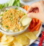 A hand scooping a potato chip into a bowl of dip.