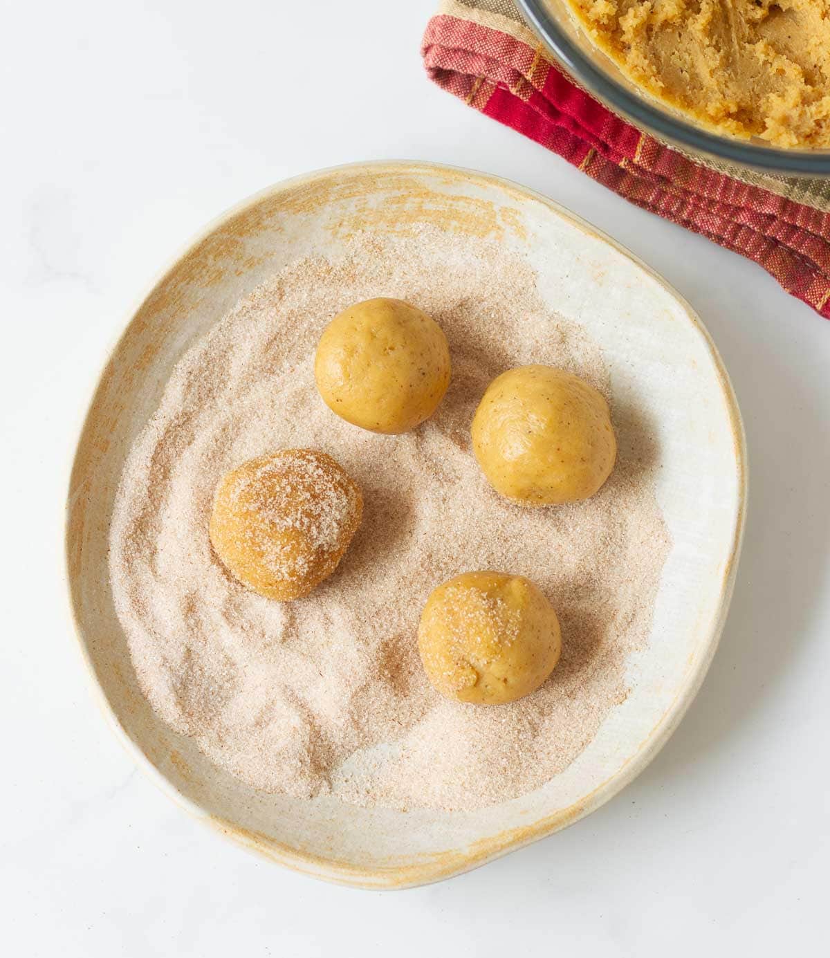 Cookie dough balls in a bowl of cinnamon sugar.