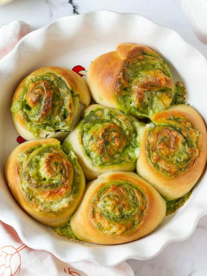 Cheesy pesto swirl rolls in a round baking dish.