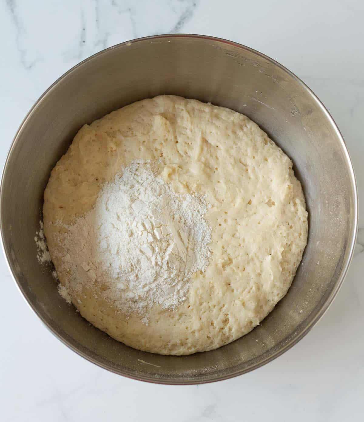 Flour on top of proofed dough in a mixing bowl.