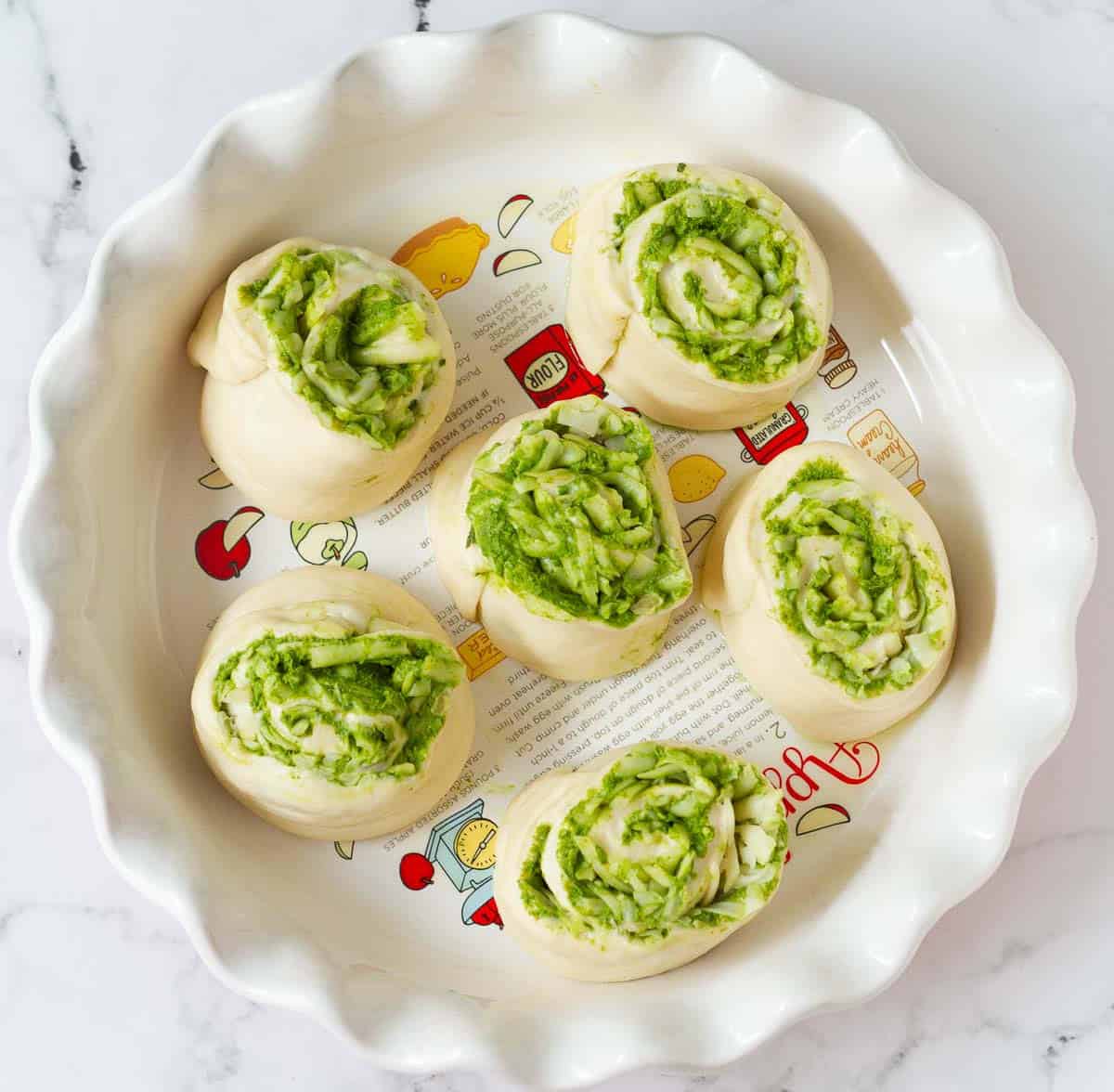 Proofed pesto rolls on a round pie baking dish.