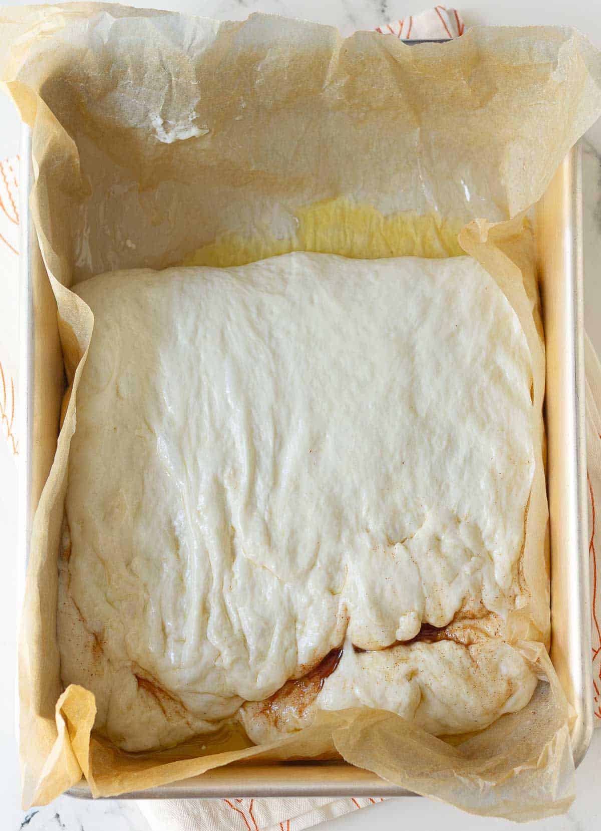 Bread dough folded over in a parchment-lined baking pan.