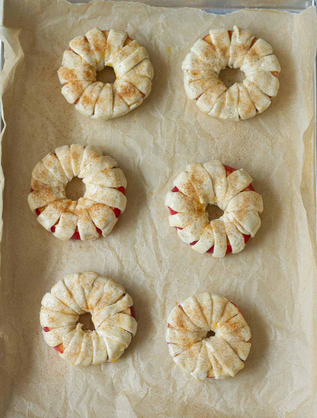 Apple rings wrapped in pastry and sprinkled with cinnamon sugar on parchment paper.