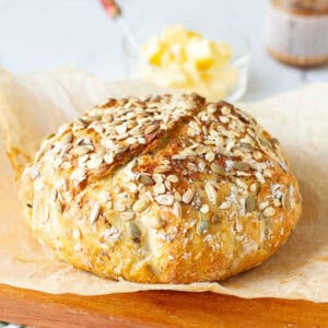 no knead seeded oatmeal bread loaf on parchment paper.