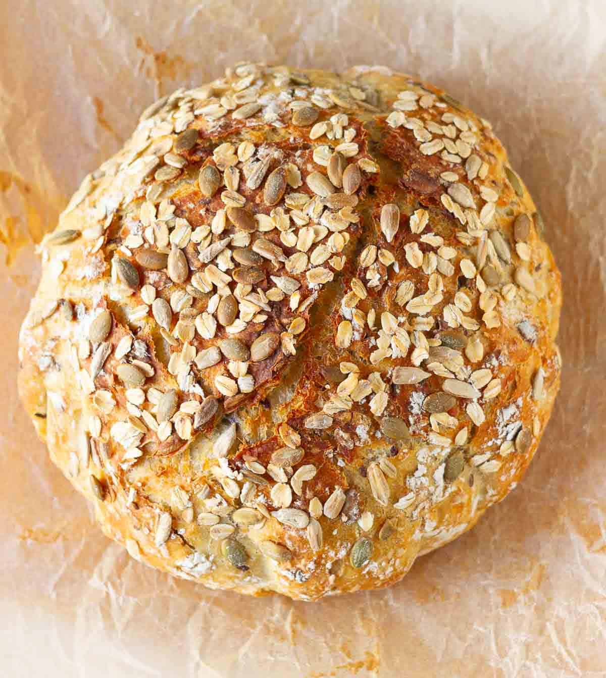 A loaf of seeded oat bread on parchment paper.