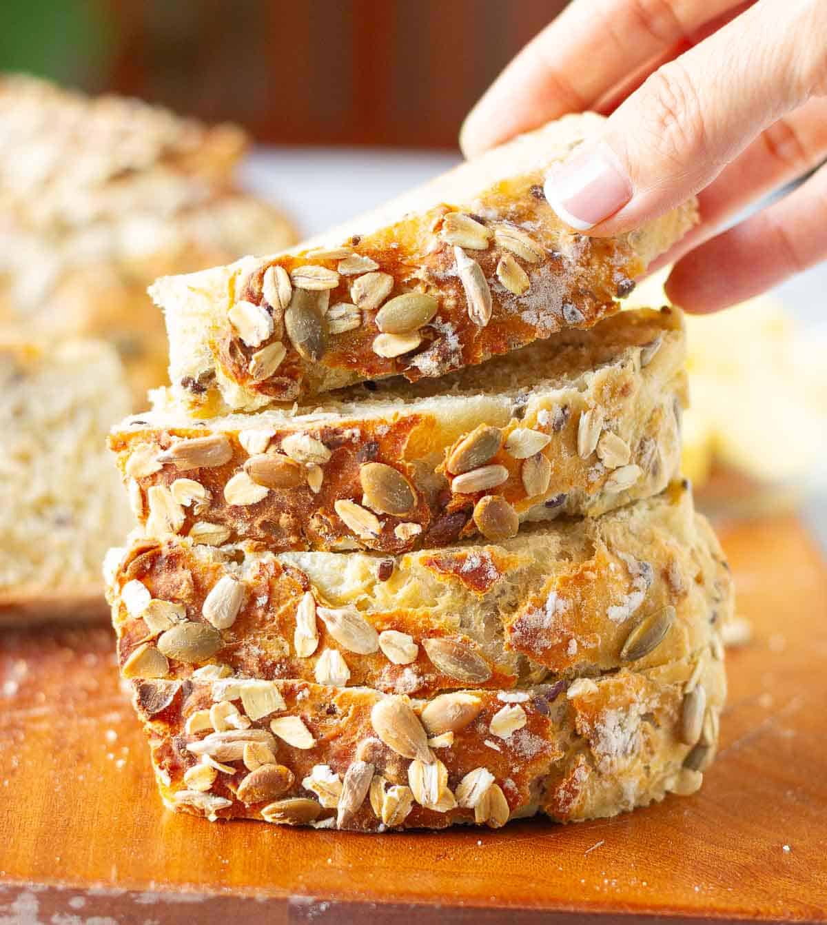 A hand picking up a slice of bread from a stack of bread slices.