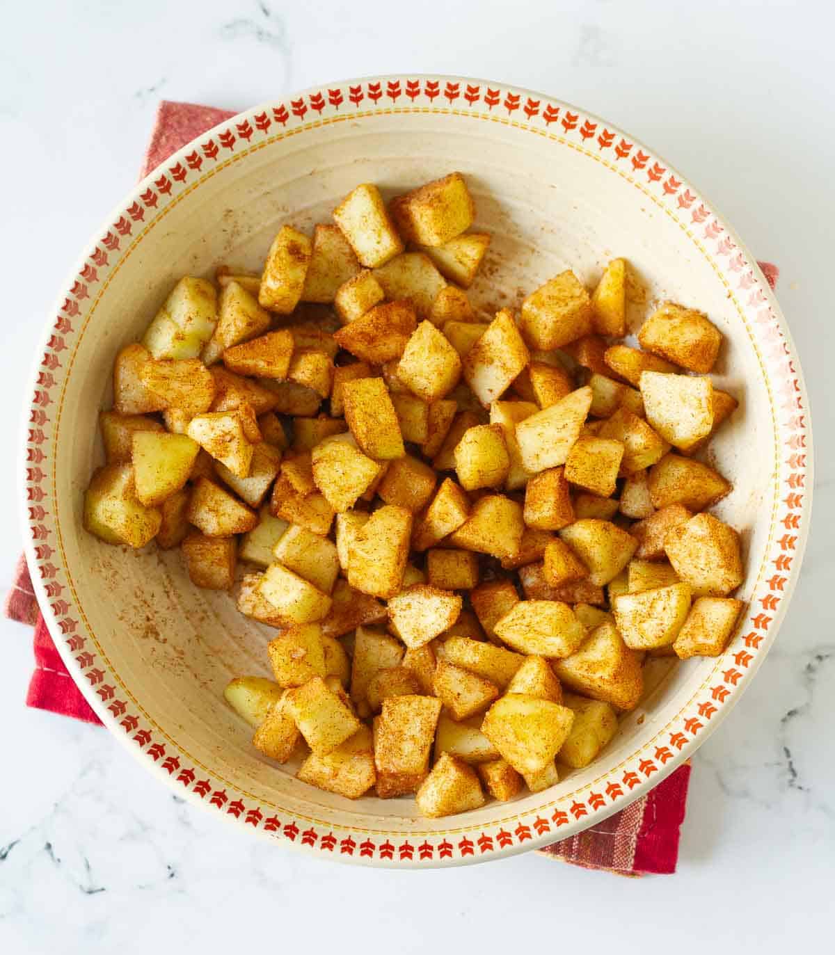 Apples tossed with sugar and cinnamon powder in a bowl.