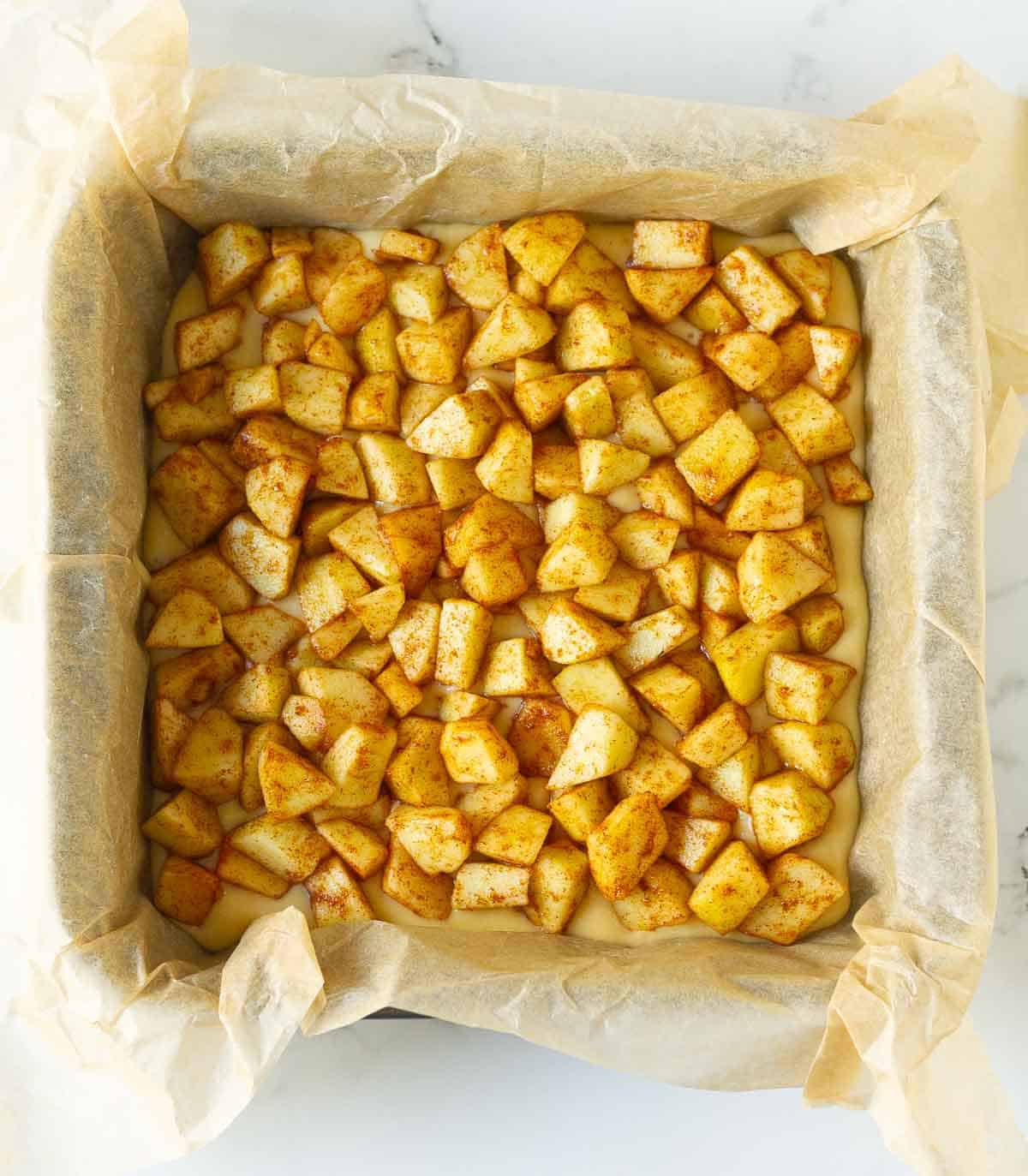 Cinnamon apples on top of cake batter in a baking pan.