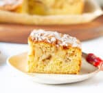 A slice of apple fritter cake on a small plate with a red fork.