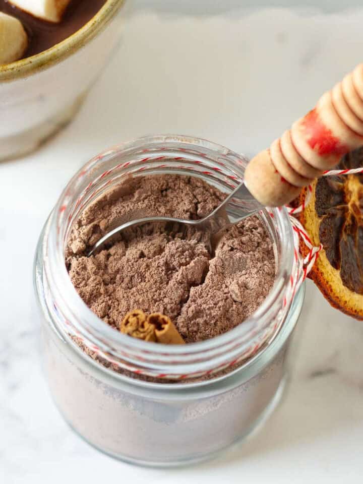 Hot chocolate mix in a jar with a spoon and twine with dried orange around it.