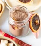 A jar of hot cocoa mix with a cinnamon stick and a twine tied around it.