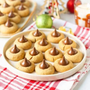 Gingerbread kiss cookies on a round serving platter with more cookies and Christmas decor in the background.