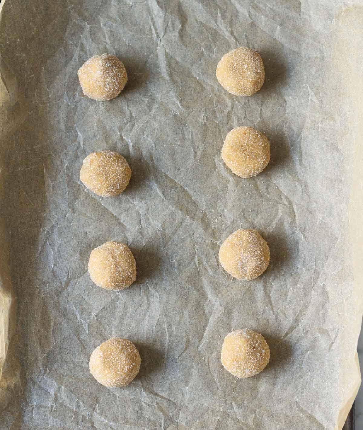 Cookie dough balls rolled in sugar on parchment paper.