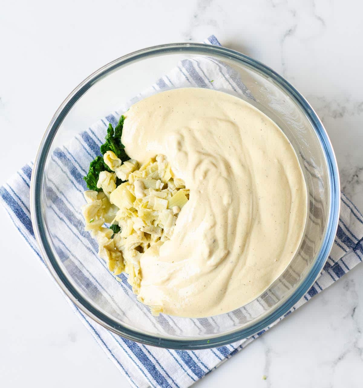 Spinach, chopped artichokes, and creamy sauce in a mixing bowl.