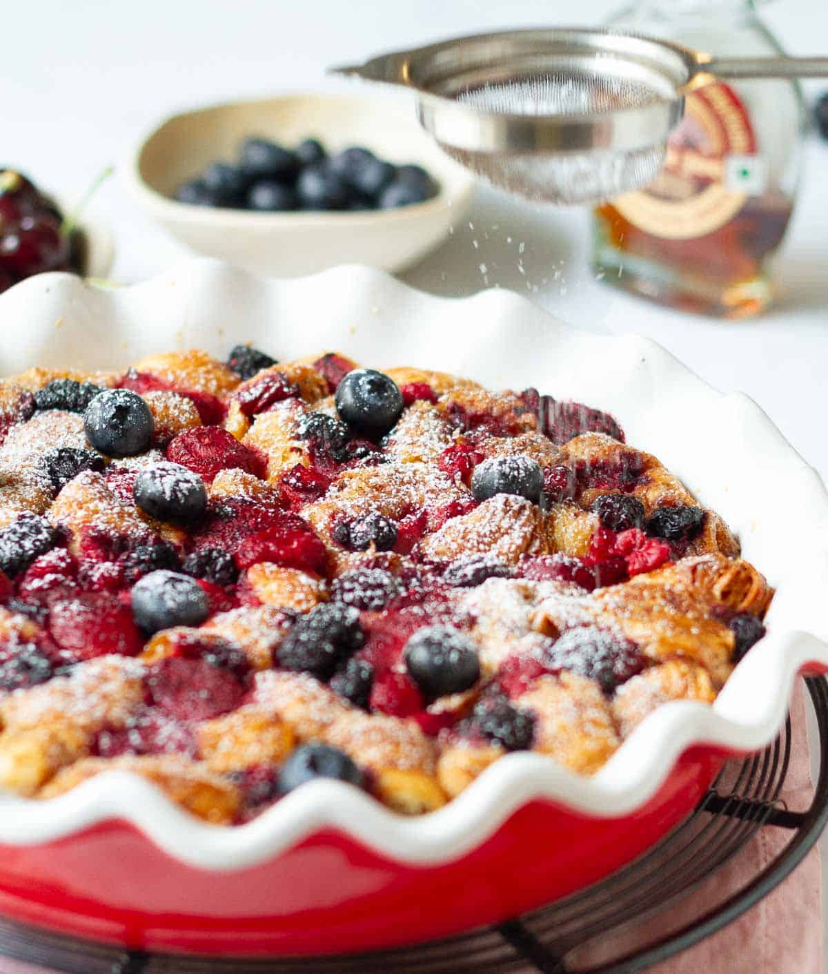 Powdered sugar getting sprinkled on baked casserole with croissants and berries.