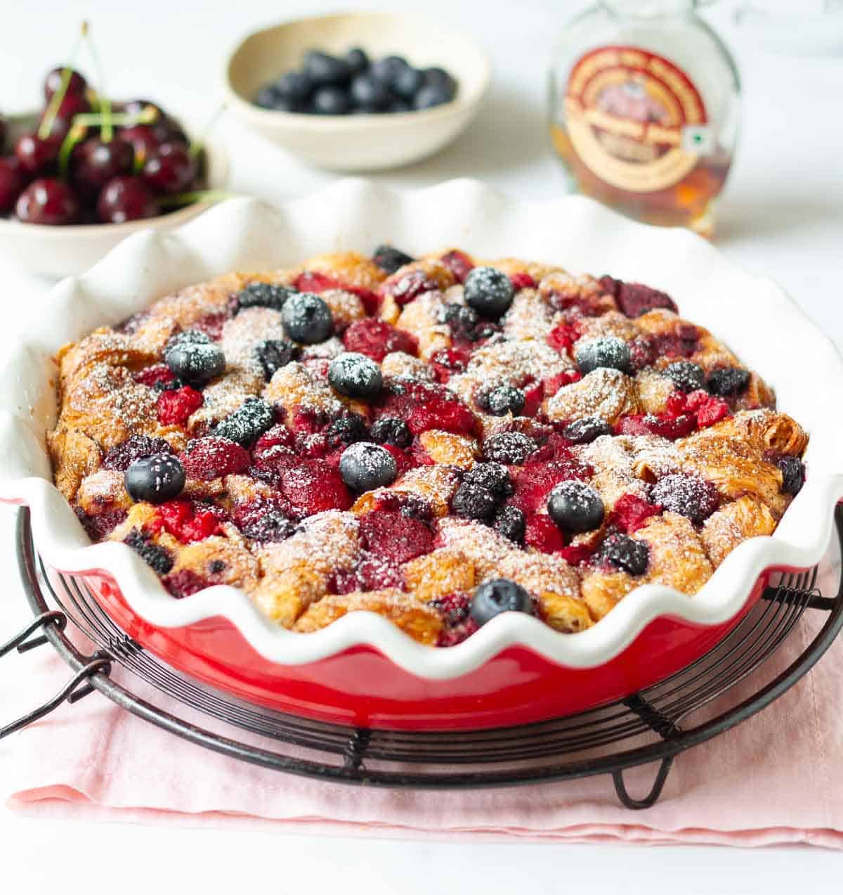 Casserole with croissants and berries in a baking dish with ingredients around.