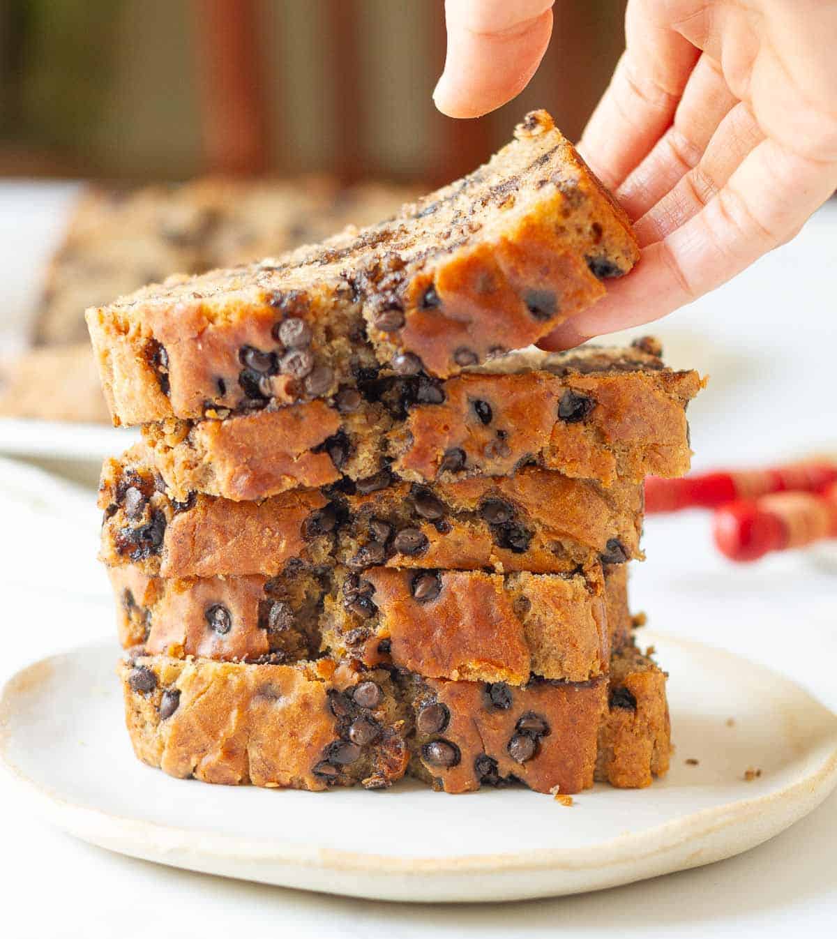 A hand picking up a slice of cake from a stack of cake slices.