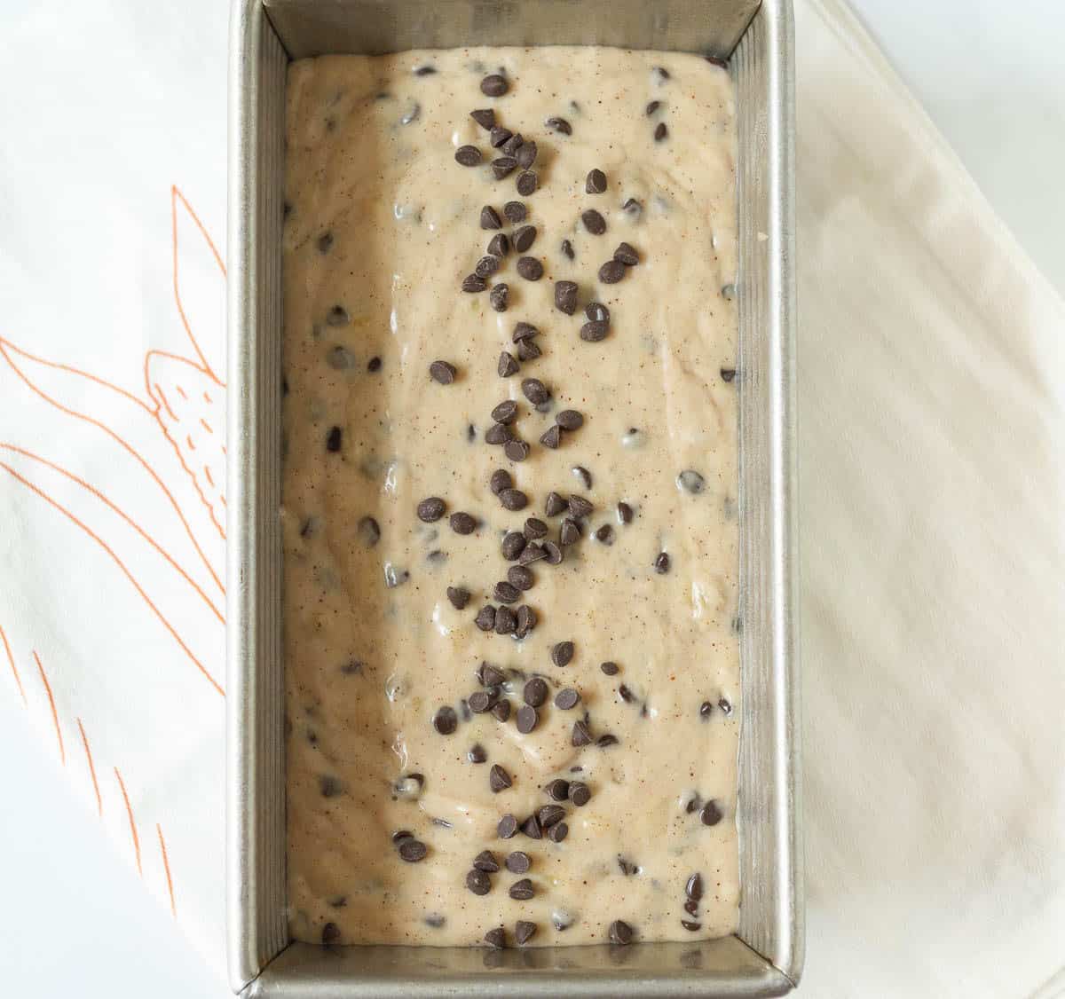 Cake batter in a loaf pan topped with chocolate chips.