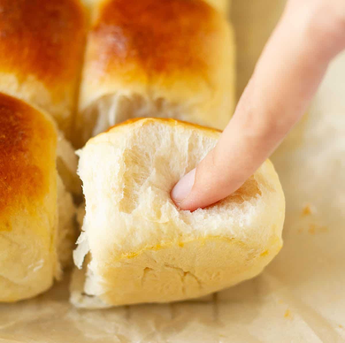 A finger pushing into a dinner roll to show the soft texture.