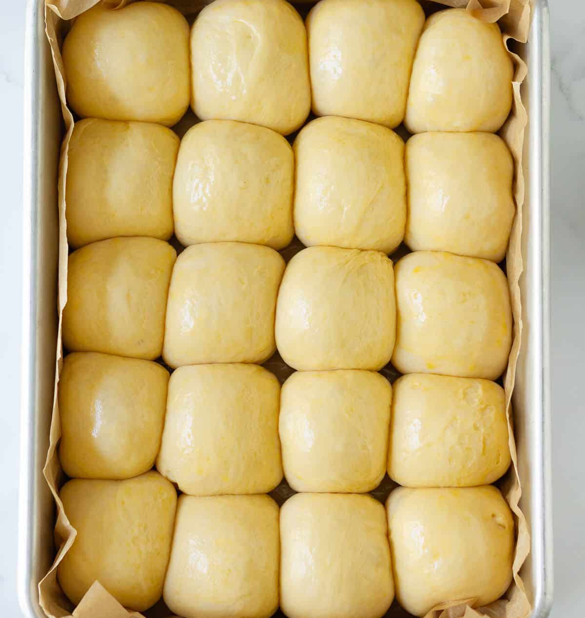 Proofed dough balls in a parchment-lined baking tray.