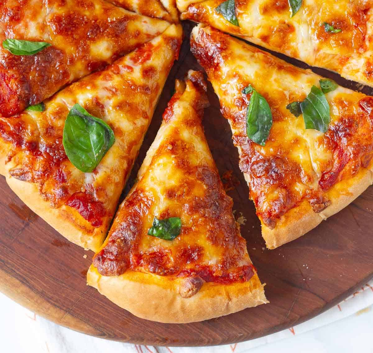 Slices of cheese pizza with basil on top on a wooden board.