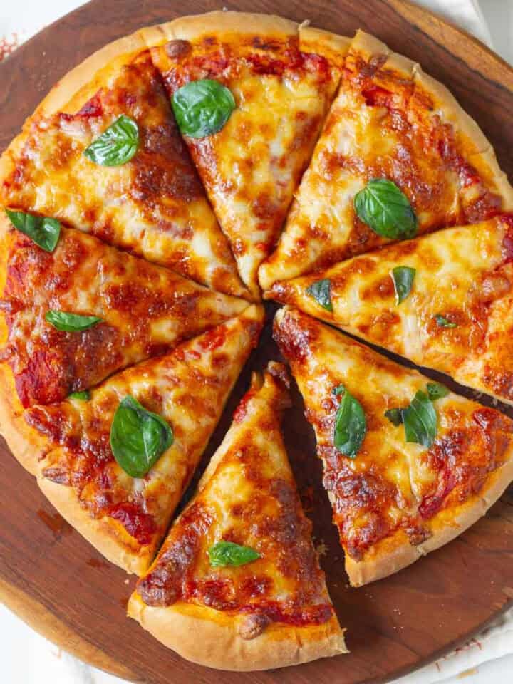 Sliced cheese pizza on a wooden board with basil leaves on top.