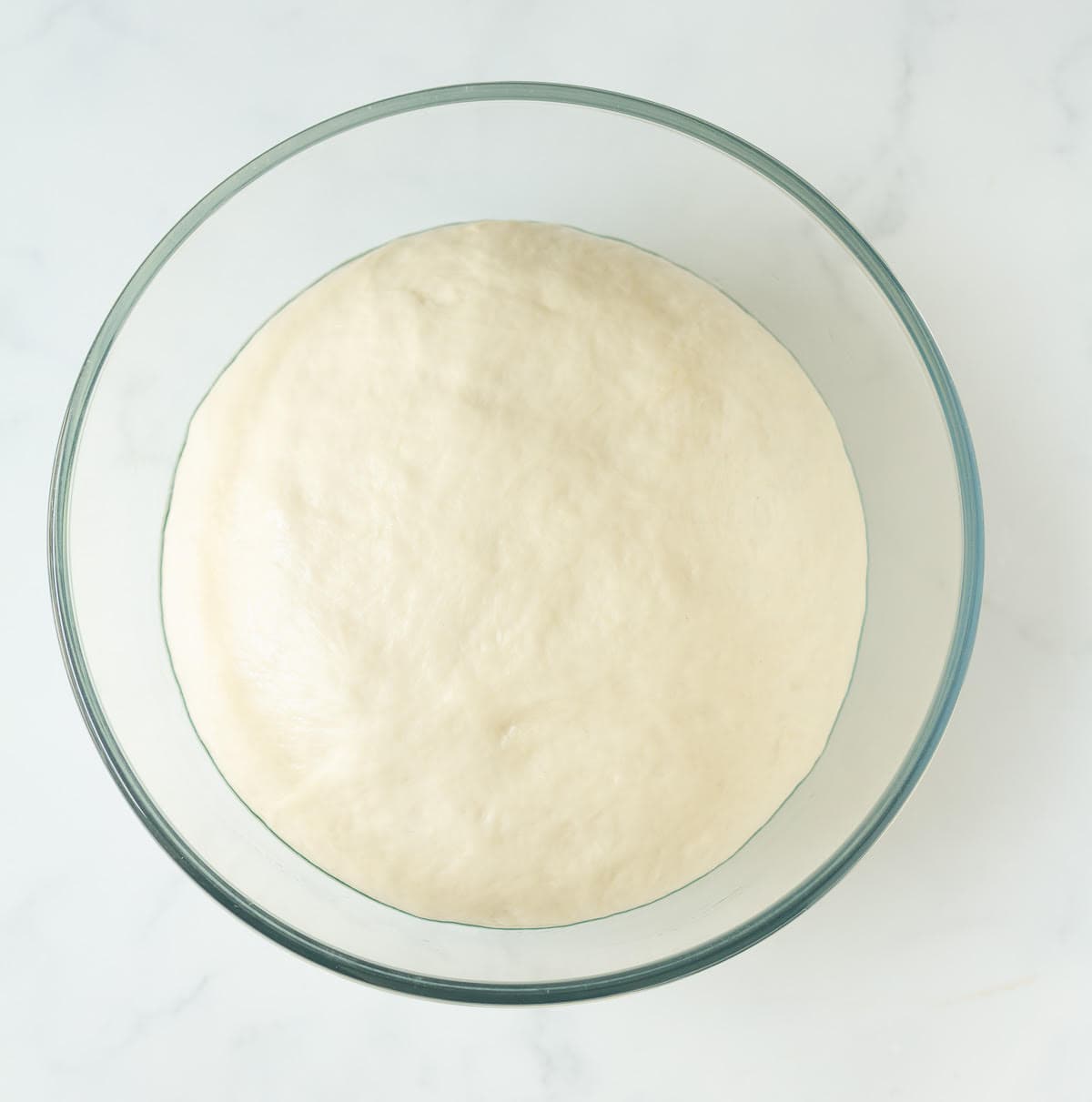 Proofed dough in a glass bowl.