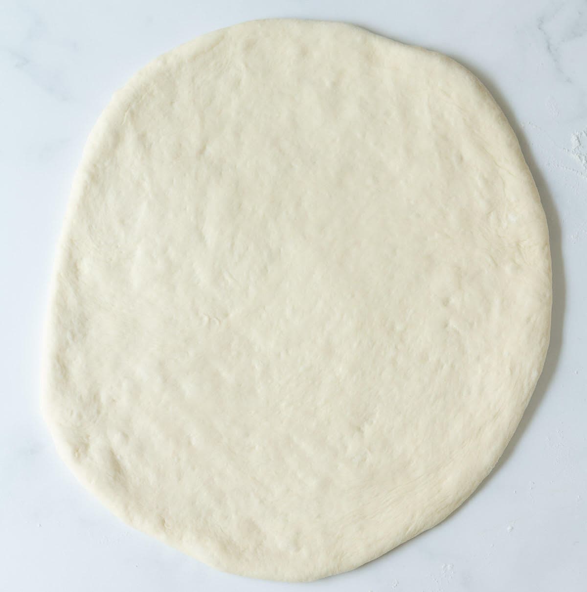 Rolled out pizza dough on a surface.